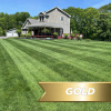 Gold LCP Promotion 28 Off 1 - Grasshopper Gardens Two-story gray house with a front porch on a well-kept lawn, surrounded by trees, under a blue sky; gold banner partially visible in foreground reading GOLD.